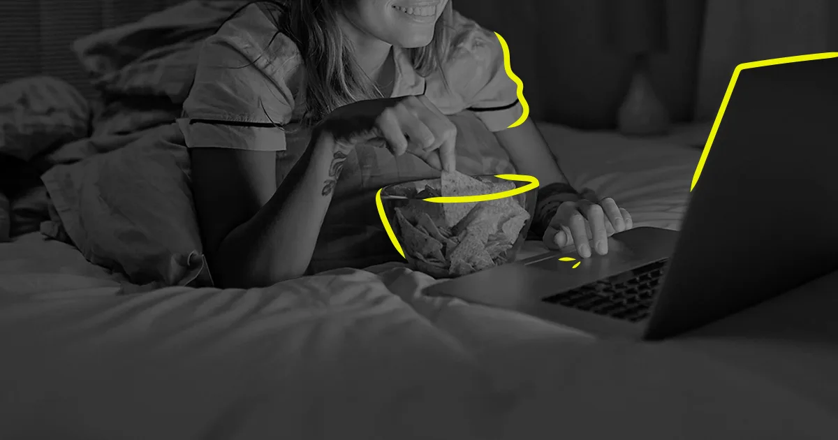 black and white image of woman streaming on her laptop on bed with snacks